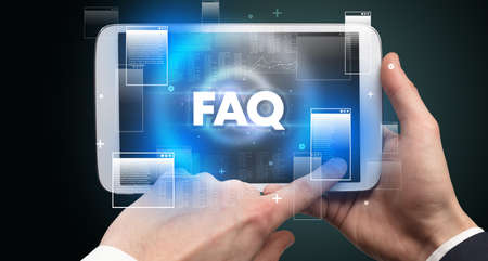 Close-up of a hand holding tablet with FAQ abbreviation, modern technology conceptの写真素材