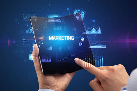 Businessman holding a foldable smartphone with MARKETING inscription, successful business conceptの写真素材