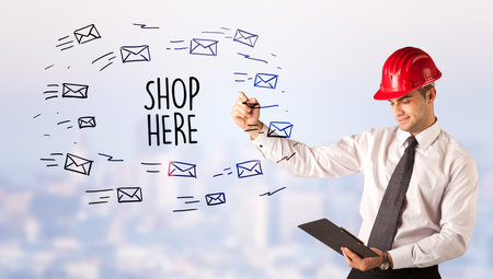 Handsome businessman with helmet drawing SHOP HERE inscription, contruction sale conceptの写真素材