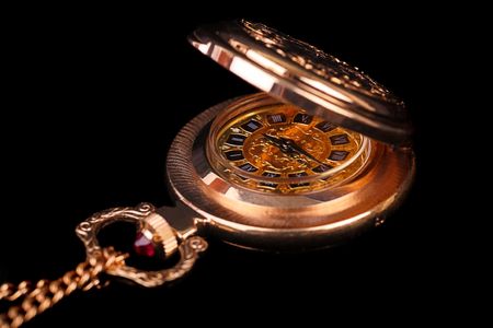 Women's gold watch with the lid open on a chain decorated with a red stone. Black background