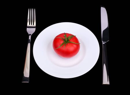 The knife, fork and fresh tomato on white plate. Black background. Isolated objectの写真素材