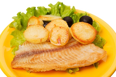 Tilapia with roasted potatoes and olives on a yellow plateの写真素材