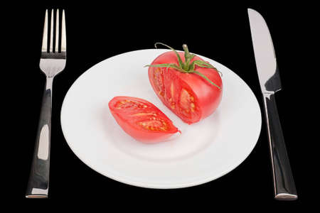 The knife, fork and fresh tomato on white plate. Black background. Isolated objectの写真素材