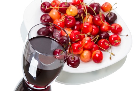A glass of cherry juice and a pile of sweet cherries on a white plateの写真素材