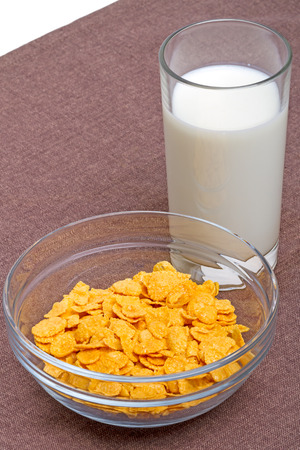 Cornflakes and glass of milk on a brown tableclothの写真素材