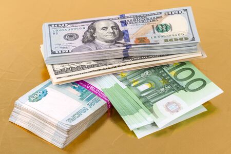 Pile of paper money (dollars, euros, russian roubles) on a gold background