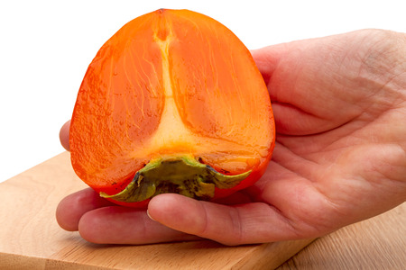 Half of a ripe persimmon in his hand on a white backgroundの写真素材