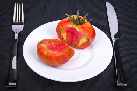 The knife, fork and fresh tomato on white plate. Black backgroundの写真素材