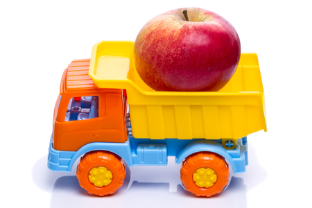 Toy plastic dumper with a fresh apple on a white backgroundの写真素材
