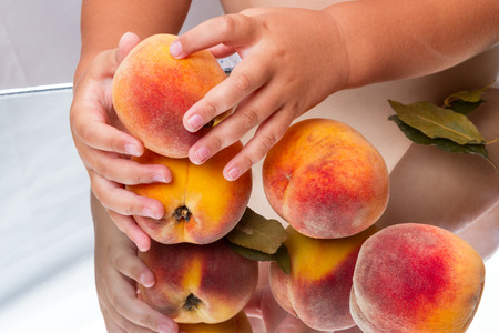 Ripe peaches and baby's hands on the mirror tableの写真素材
