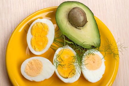 Four halves of boiled eggs and avocado on a yellow plate. Egg with two yolksの写真素材