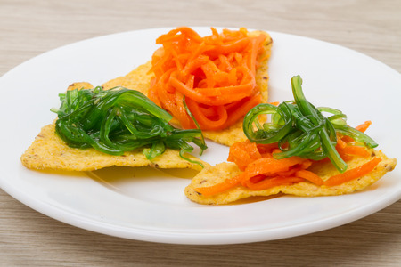 Chips with seaweed salad and carrots on a white plateの写真素材