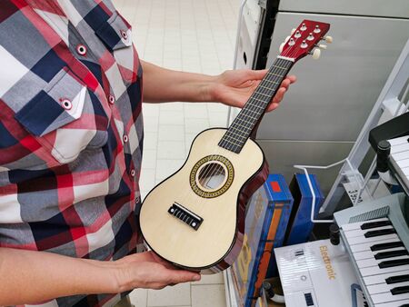 Little six-string guitar in the hand of a woman in the storeの写真素材