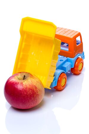 Toy plastic dumper with a fresh apple on a whiteの写真素材