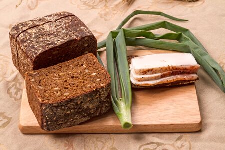 Pieces of brackish bacon with rye bread and green onions on the table