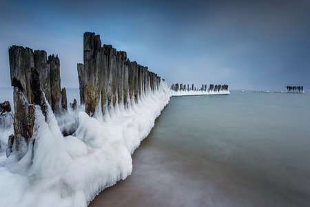 Winter landscape at the sea. Frozen wooden breakwaters line to the world war II torpedo platform at Baltic Sea. Morning at Babie Doly, Poland. Long exposure photo.の写真素材