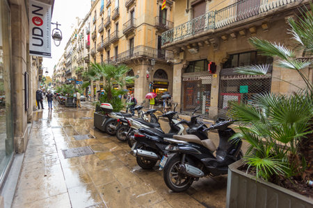 Barcelona, Spain- 09 November 2014: Carrer dels Flassaders, narrow, wet street at the center of the town, parking for motorbikes. Historic tenement house with shops and restaurants.のeditorial素材