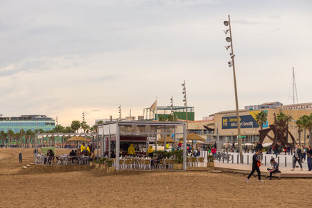 Barcelona, Spain- 09 November 2014: Restaurants and people on the most fashionable Barceloneta Beach. Modern building in the background.のeditorial素材