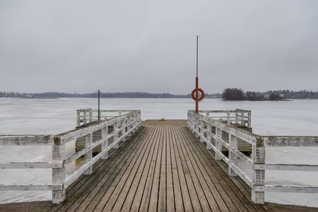 Small pier at beach with red lifebuoy in Seurasaari island. Baltic coastline. Winter landscape in Finland.の写真素材