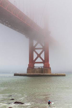 San Francisco, California, USA- 08 June 2015: The Golden Gate Bridge in foggy weather, man floating on a board under the bridge. The most popular place in the town.のeditorial素材
