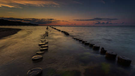 Sunset landscape at the sea. Wooden breakwaters line to the world war II torpedo platform at Baltic Sea. Morning at Babie Doly, Poland. Long exposure photo, Gdynia, Poland.の写真素材