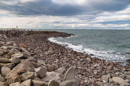 Rocky coast of Faxafloi Bay, lighthouse in the background. Seltjarnarnes, Reykjavik, Iceland.