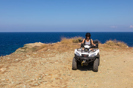 Folegandros Island, Greece - 25 September 2020: Woman with black helmet on quad bikes on a countryside trail. Gravel road along the coast on the island of Folegandros.のeditorial素材
