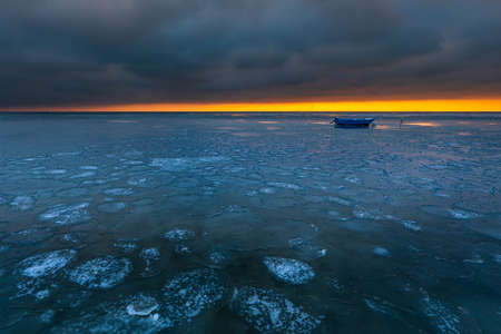 Boat moored on the frozen Gdansk Bay in Jastarnia. Beautiful sunset, winter landscape. Poland.