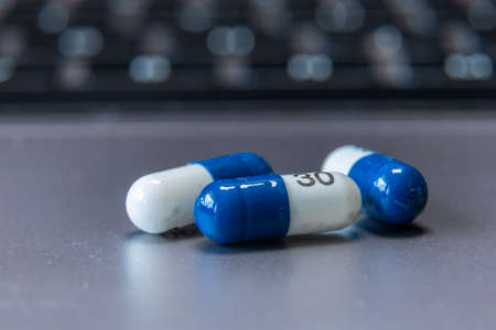 Blue and white tablet pills on a gray table. Healthcare medical. Computer keyboard in the background.の写真素材