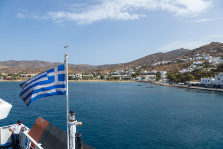 Ios Island, Greece- 26 September 2020: View of the harbor of Ios Island. Greek flag on the side of the ferry. Traditional white building on the hills.のeditorial素材