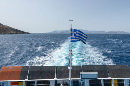Ios Island, Greece- 26 September 2020: View of the harbor of Ios Island. Greek flag on the side of the ferry. Traditional white building on the hills.のeditorial素材