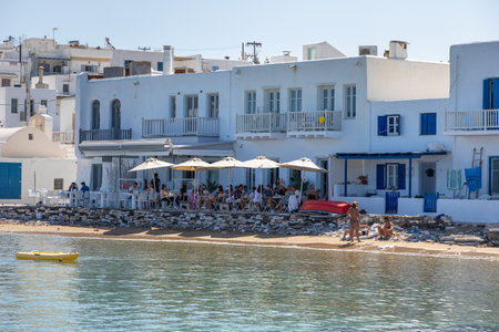 Naoussa, Paros Island, Greece - 27 September 2020: View of the small port town on the island of Paros. People in the restaurant and on a beach. White traditional villas with blue shutters.のeditorial素材