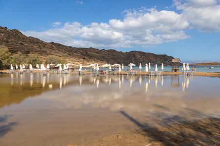 Monasteri Beach, Paralia, Paros Island, Greece - 27 September 2020: One of the most popular beach on Paros. People sunbathing on the sun loungers under white umbrellas.のeditorial素材