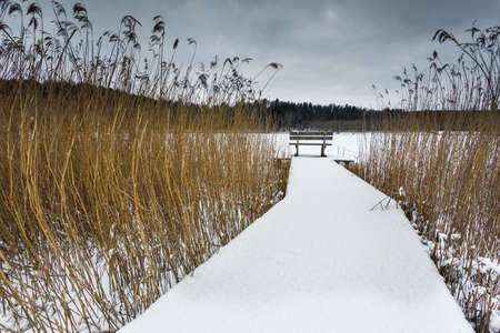 Small woody fishing pier at the lake in winter season. Moody cloudy day.Okuniewo, Pomeranian Voivodeship, Poland.の写真素材