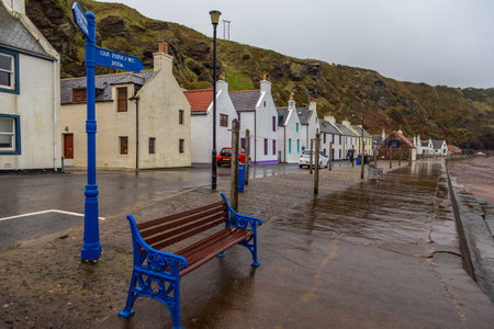Pennan, Aberdeenshire, Scotland, UK - February 05, 2016: Quayside benches overlooking the North Sea. Historic houses in the background. Rainy day.のeditorial素材