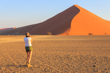 Sossusvlei, Namibia 29 September 2018: A woman taking a photo of the dunes in the southern part of the Namib Desert in the Namib-Naukluft National Park of Namibia. Beautiful sunset.のeditorial素材