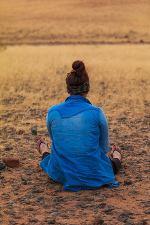 Solitaire, Namibia - 01 October 2018: A girl sitting on earth. Sunset over the savannah.