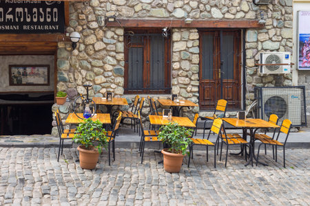 Georgia, Tbilisi - August 30, 2019: Tables in the garden of the restaurant. Stone facade traditional houses in the Old Town of Tbilisi. capital city.のeditorial素材