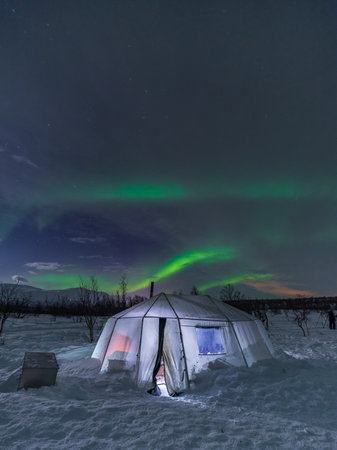 Aurora Borealis, Northern Lights, at Abisko National Park. Lighted tent in the snowing glade. Lapland, Sweden.の写真素材