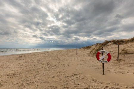 Empty sandy beach with lifebuoy and cloudy sky in Sandhammaren, Sweden. Coastal safety scene.の写真素材