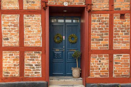 Close-up of a blue door with decorative wreaths in a traditional red brick and timber-framed house...