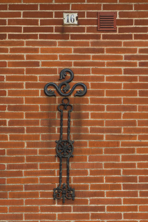 Decorative black ironwork mounted on a red brick wall with number 16 in Ystad, Sweden.の写真素材