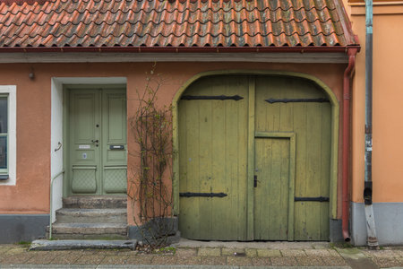 Rustic green gate and light green door on a pastel orange house facade in Ystad, Sweden.の写真素材