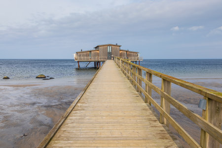 Wooden seaside bathhouse on stilts at the shore in Torekov, Sweden. Calm day with cloudy sky and low tide.の写真素材