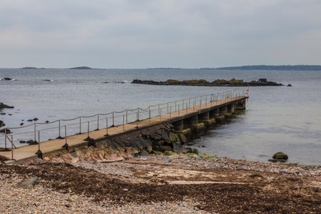 Long stone pier with railing stretches into calm sea in Torekov, Sweden on a cloudy day.の写真素材