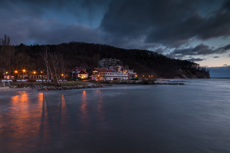 Orlowo beach and cliffs in Gdynia, Poland. Lights reflect on the sea during calm twilight.の写真素材