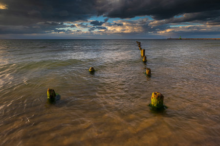 Old wooden posts stretch into the Baltic Sea under dramatic clouds, northern Poland.の写真素材