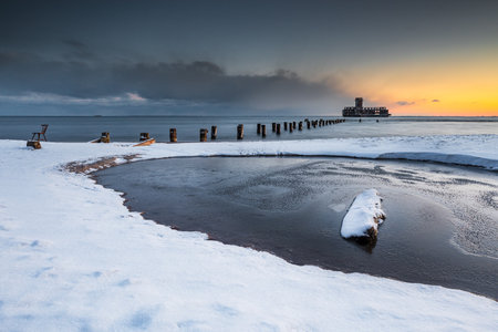 Snow-covered beach and frozen shore with pier remains and torpedo station in Babie Doly, Gdynia, Poland.の写真素材
