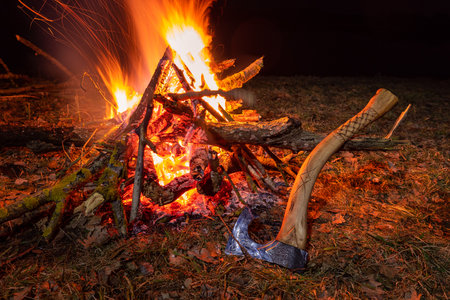 Glowing campfire in the forest near Biebrza River, with a handmade ax resting on the ground  warm outdoor night scene.の写真素材