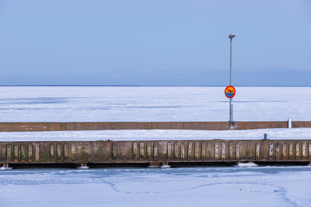 Winter scene in Puck, Poland. A snowy pier stretches over the frozen sea under a clear sky and modern streetlamp.の写真素材
